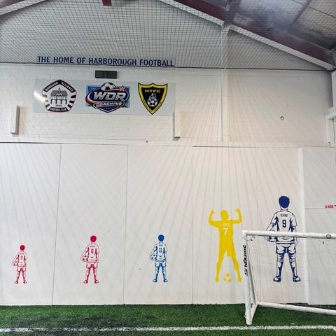 The arena wall lettered “The home of Harborough football”, with the Borough Alliance, WDR Coaching and Harborough Town crests and the painted player figures below
