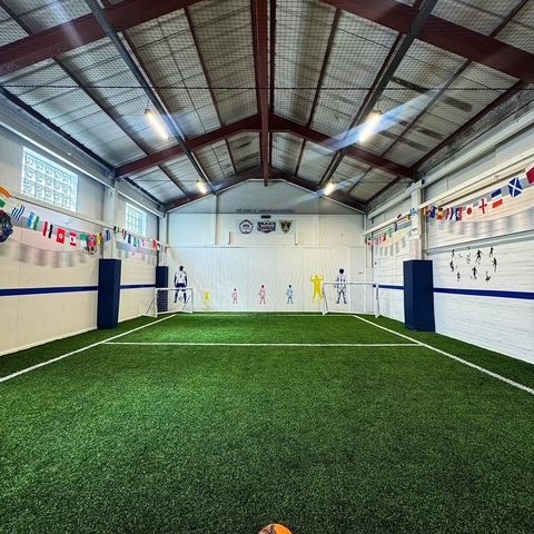 The empty astro pitch end to end, a ball on the centre line, the flags of the world along both walls and the pitched roof above