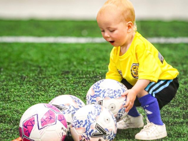 Young children playing football indoors at a First Kicks session
