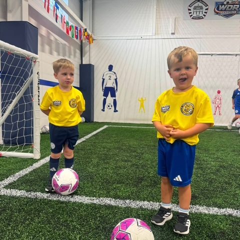 Two toddlers in yellow HTFC Bumblebees First Kicks shirts standing with a ball each in front of the goal