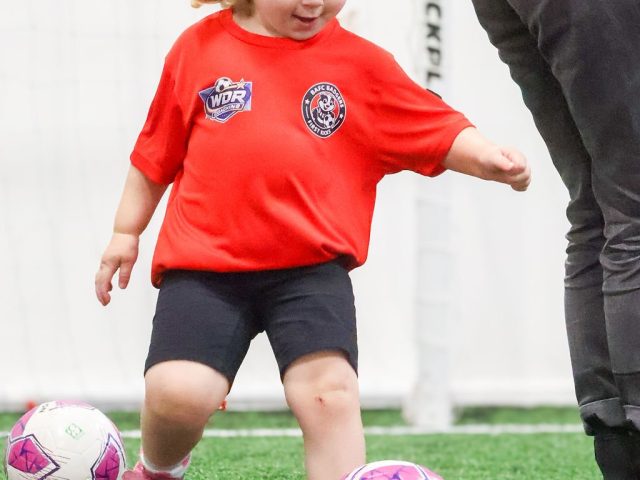 A young girl in a red BAFC Badgers shirt swinging a leg at a pink football