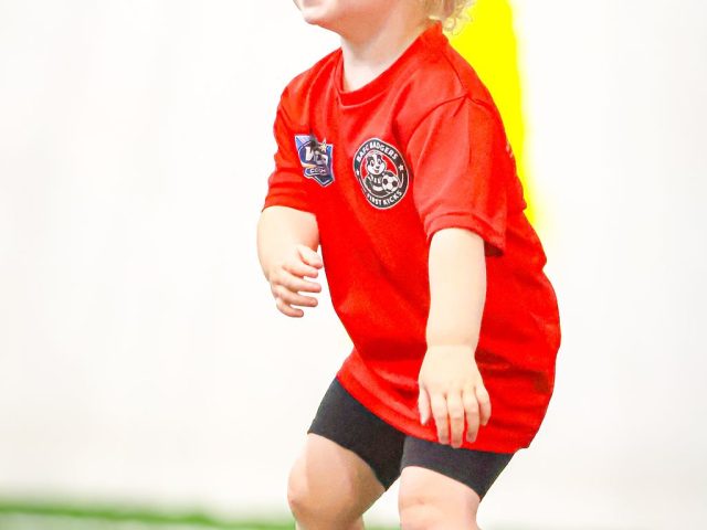 A young girl in a red BAFC Badgers First Kicks shirt stood ready, looking across the pitch