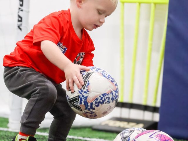 A boy in a red BAFC Badgers shirt lifting a football beside a FORZA free-kick mannequin