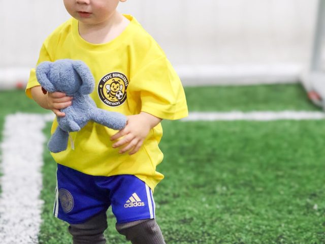 A toddler in a yellow HTFC Bumblebees shirt walking off with a toy elephant under his arm
