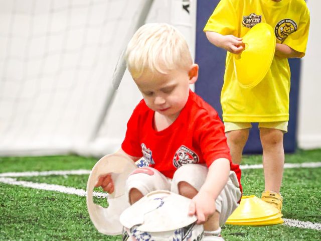 Two young children collecting up marker cones and footballs at the end of a session
