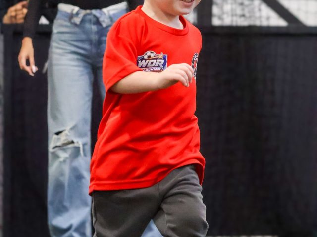 A toddler in a red WDR Coaching shirt running towards the camera, grinning