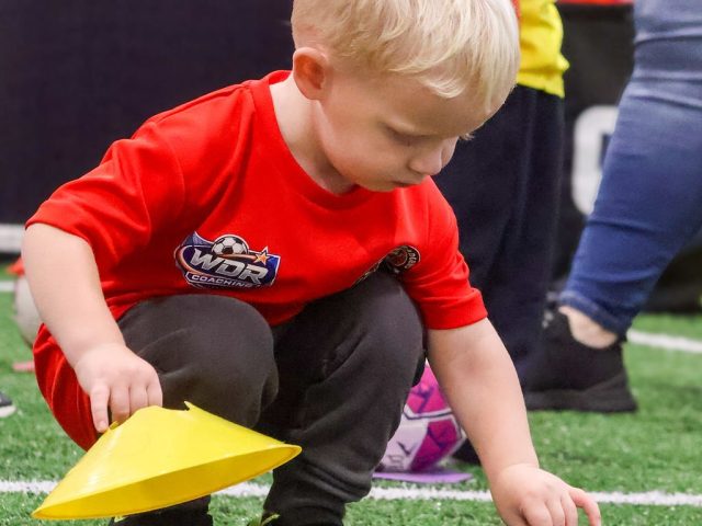 A boy in a red WDR Coaching shirt stacking yellow and blue marker cones