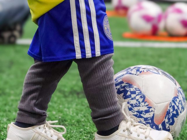 A close view of a toddler's trainers beside a Mitre ball on the astro
