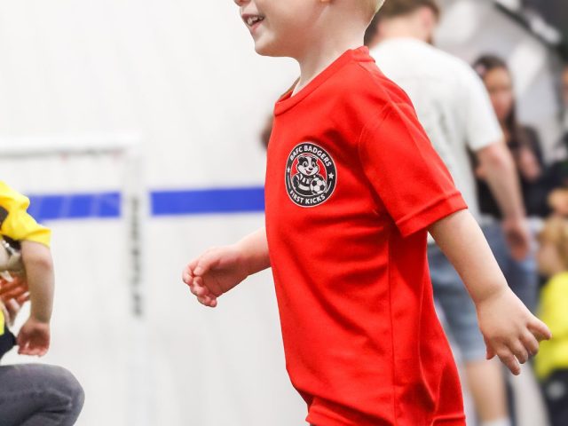 A boy in a red BAFC Badgers shirt walking up to a Mitre ball