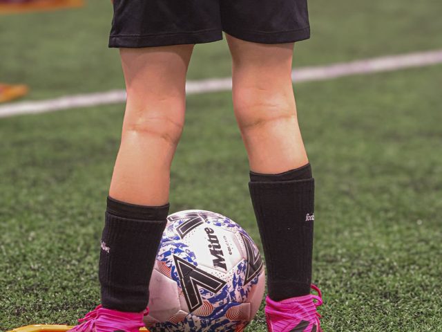 A player standing over a Mitre ball in pink boots, inside a marker ring