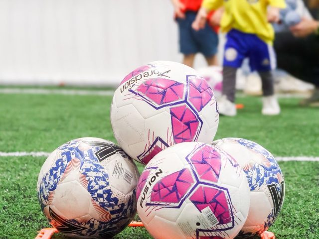 Four footballs stacked in an orange marker ring on the astro, a session going on behind
