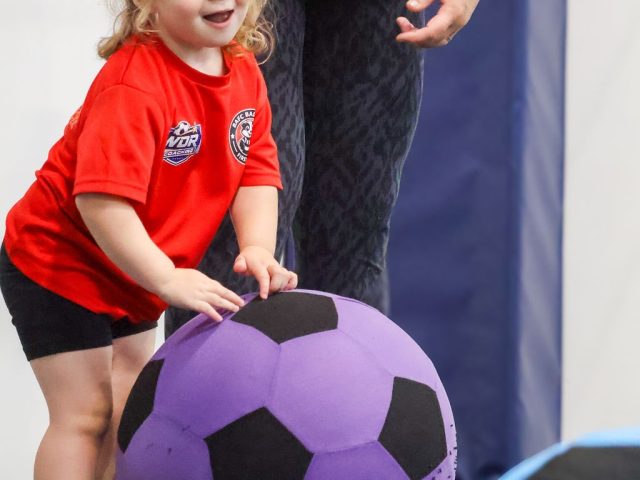 A young girl in a red BAFC Badgers shirt pushing a giant purple football