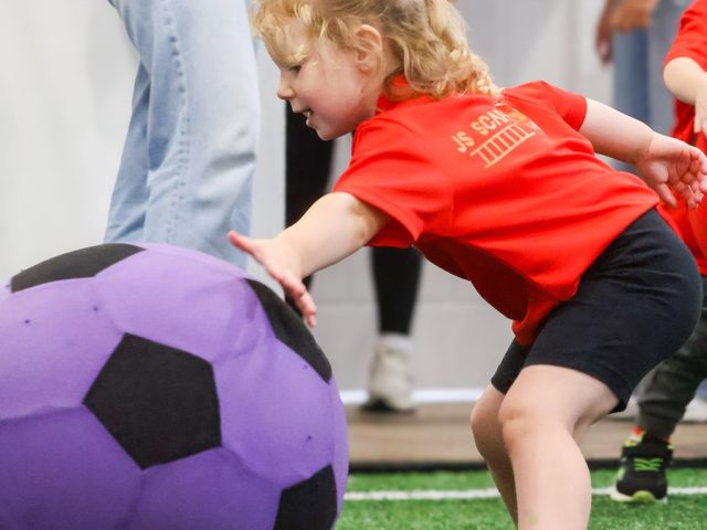 A young girl in a red JS Scaffolding Services shirt reaching out for a giant purple football