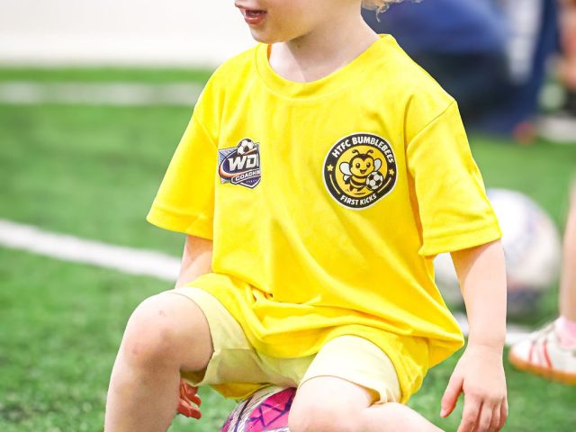 A boy in a yellow HTFC Bumblebees shirt walking a giant purple football past the FORZA mannequins