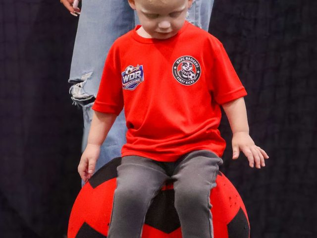 A child in a red BAFC Badgers shirt sitting on a giant red football