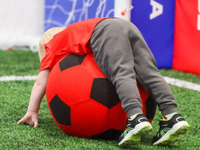 A child tumbling head first over a giant red football in front of the goal