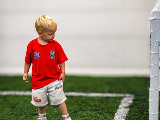 A young player in a red BAFC Badgers shirt walking across the goalmouth