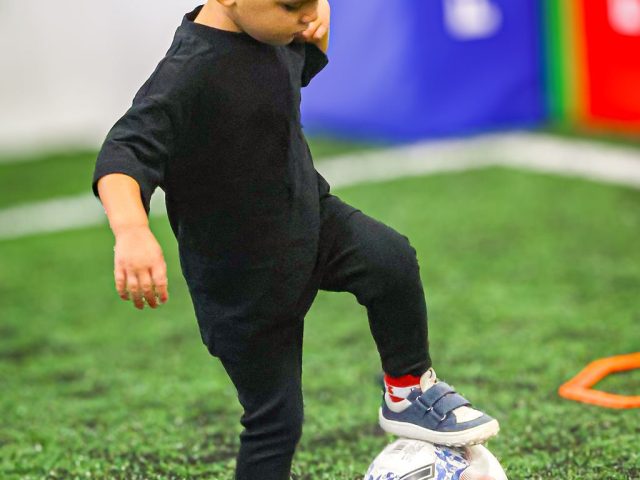 A young player in black resting a foot on a Mitre ball