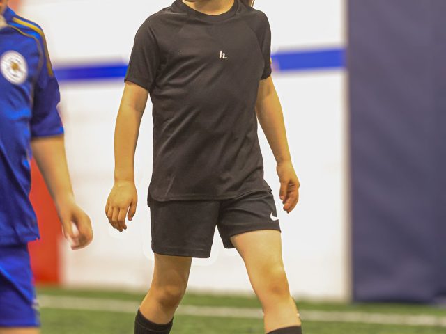 A girl in black kit dribbling a ball across the astro