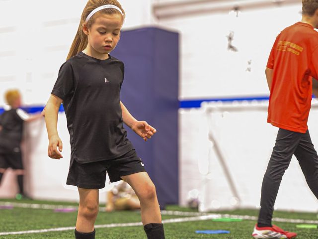 A girl in black kit knocking a ball forward across the astro