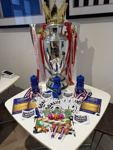 The Premier League trophy on a table with WDR goodie bags, water bottles, medals, party horns and colouring sheets laid out ready