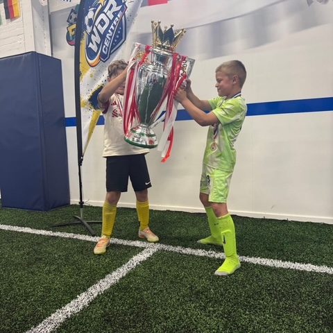 A young goalkeeper in a green kit holding the Premier League trophy on the pitch