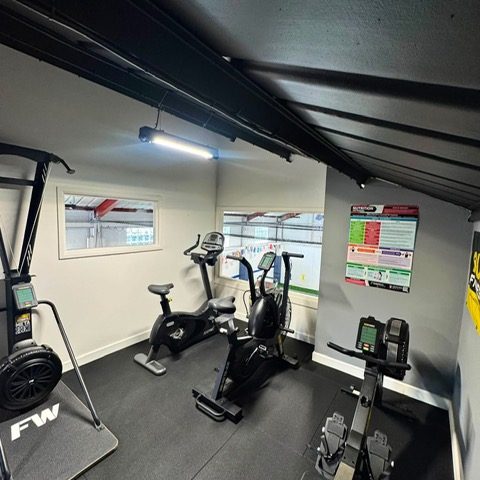 The cardio corner of the studio gym — exercise bikes, a rower and a cross trainer beneath the windows
