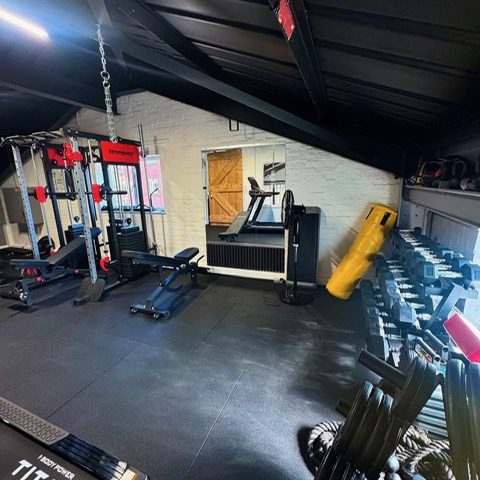 The squat rack, benches and treadmill end of the studio gym, with dumbbells racked along the wall