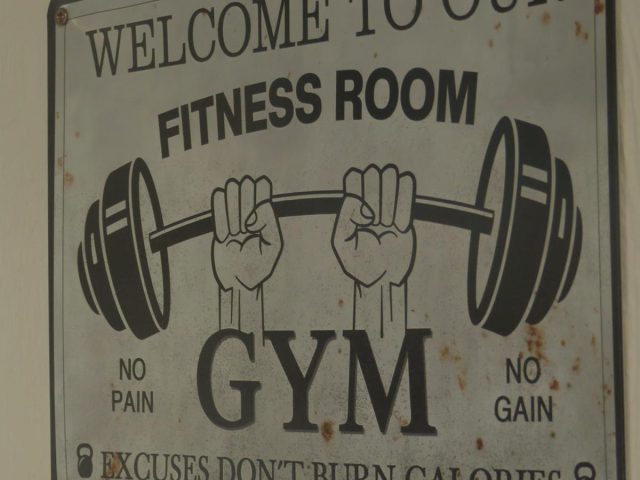 A metal sign on the studio gym wall reading “Welcome to our fitness room gym”